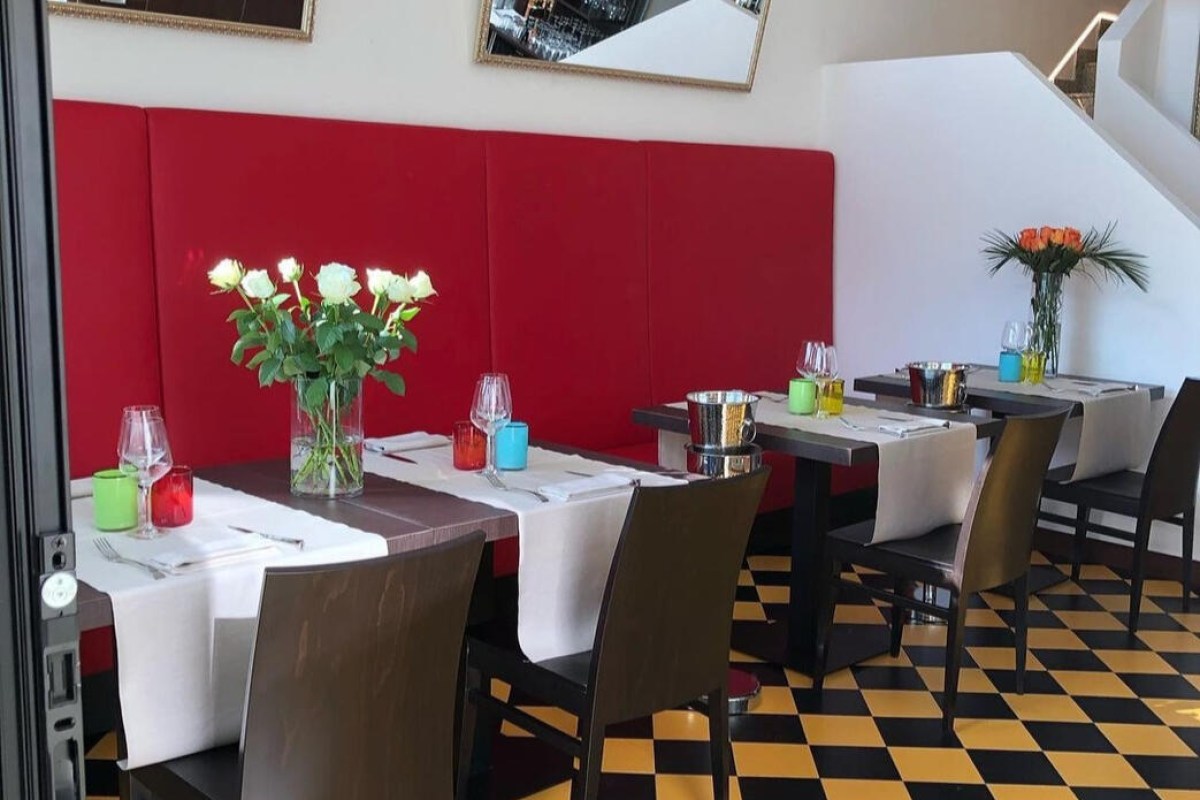 Restaurant dining room with red bench seating, set tables with white cloths and colorful glassware, checkered floor