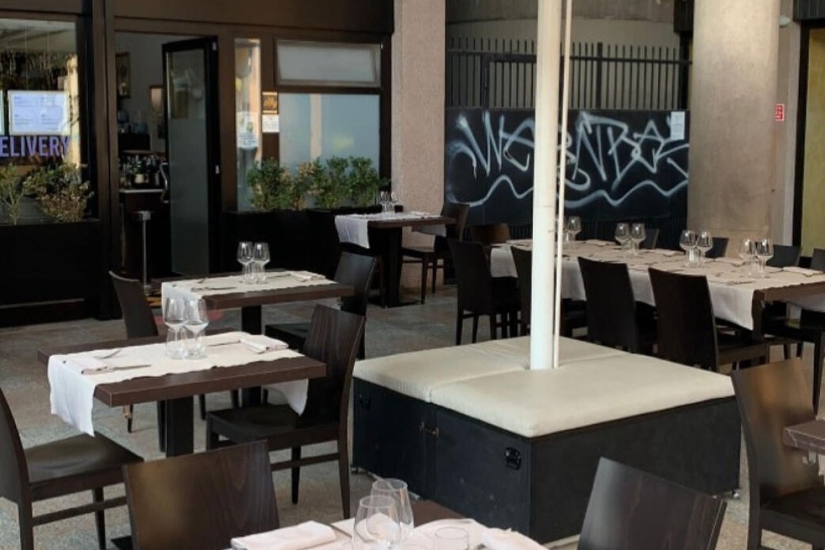 Outdoor terrace dining area with set tables, chairs, and umbrella stand near restaurant entrance