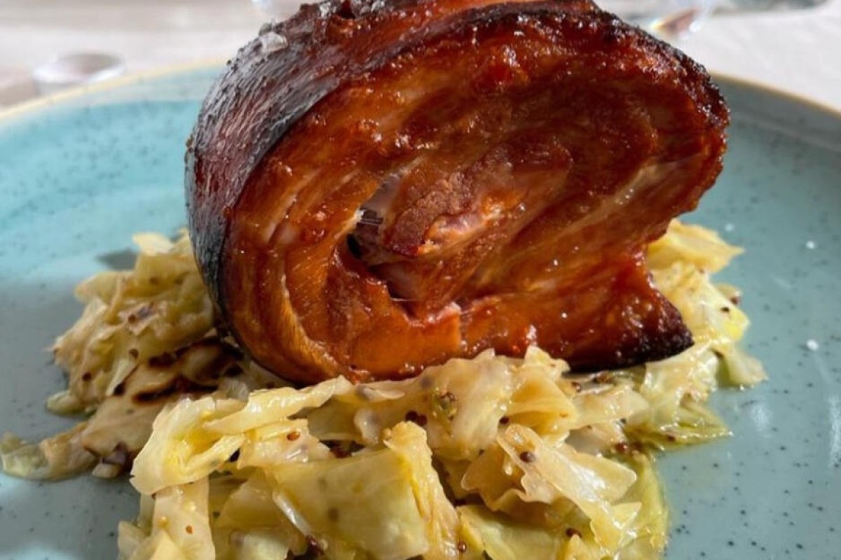 Plated pork roll dish served on a shredded cabbage slaw with mustard seeds on a blue plate