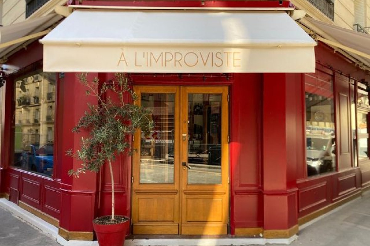 Exterior of À L'Improviste restaurant with red facade, wooden door and awning bearing its name