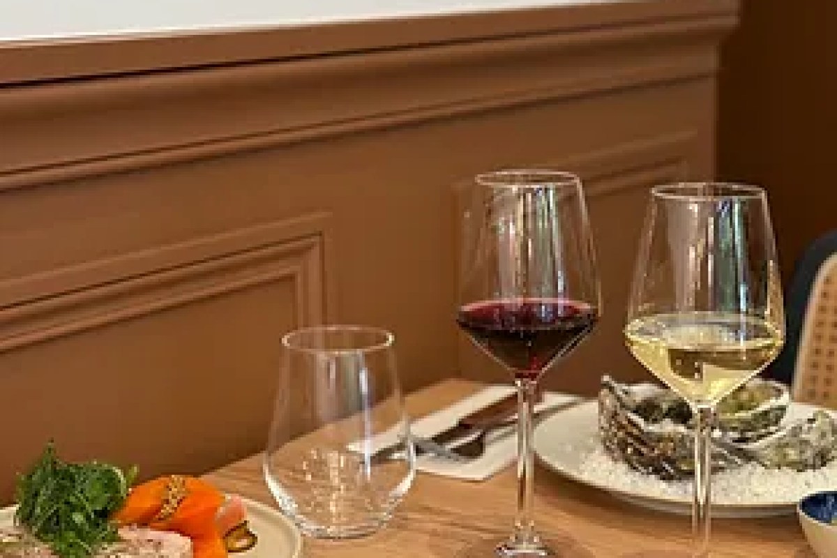Close-up of a dining table with red and white wine glasses and a plate of oysters against a brown paneled wall.