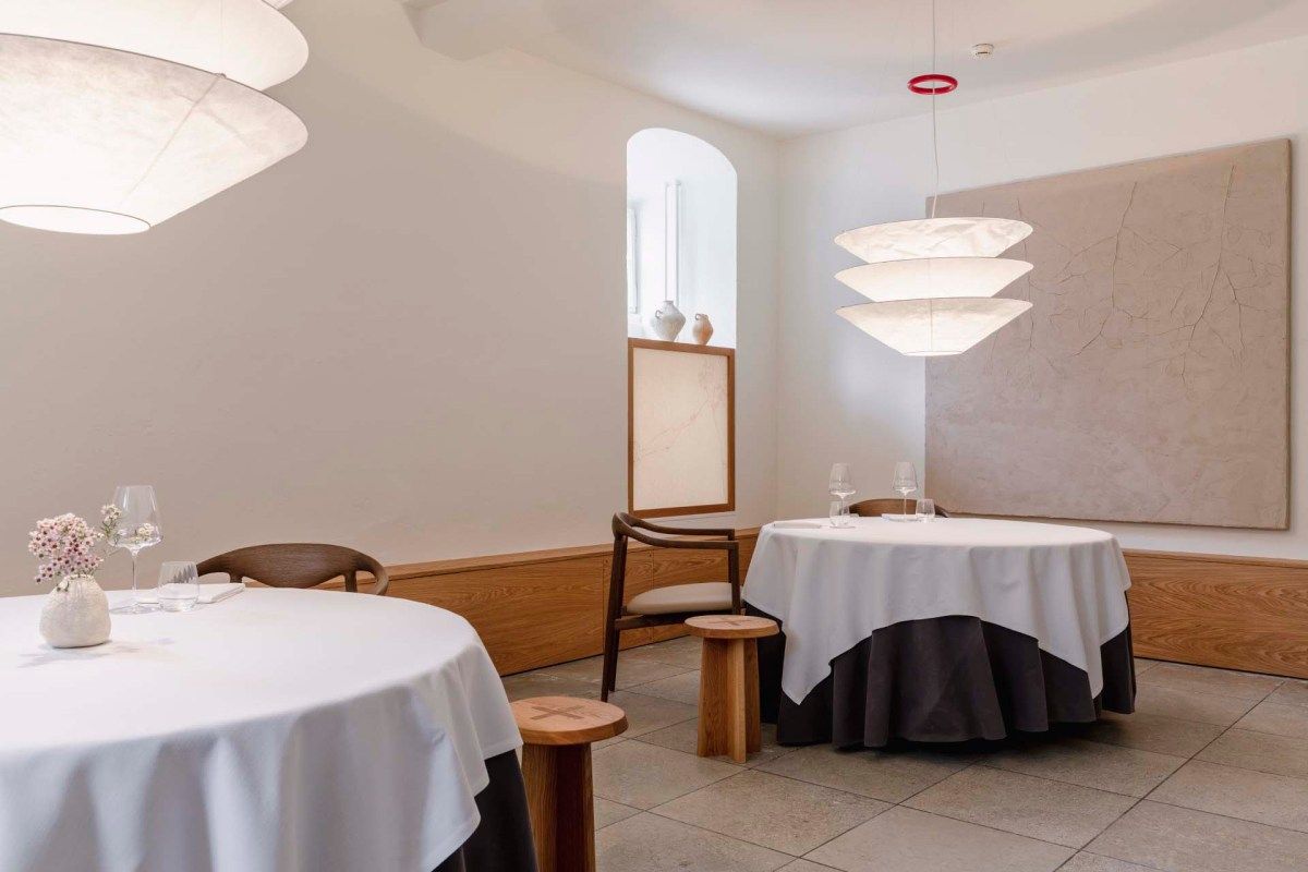 Dining room with vaulted ceiling, two set tables with white and dark linens, pendant lamps