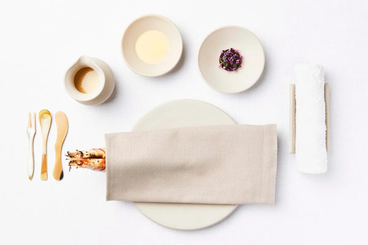 Overhead view of an artfully arranged tasting course with small dishes, cutlery and napkin