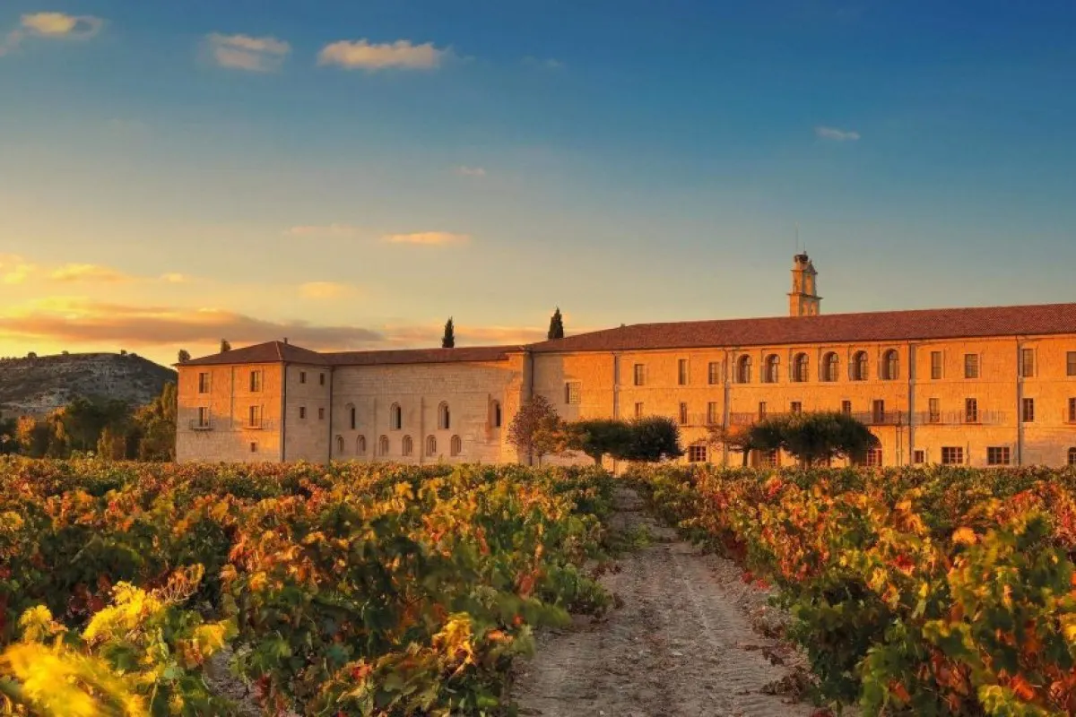 Historic stone monastery building of Abadía Retuerta at sunset with vineyards in foreground and a tower
