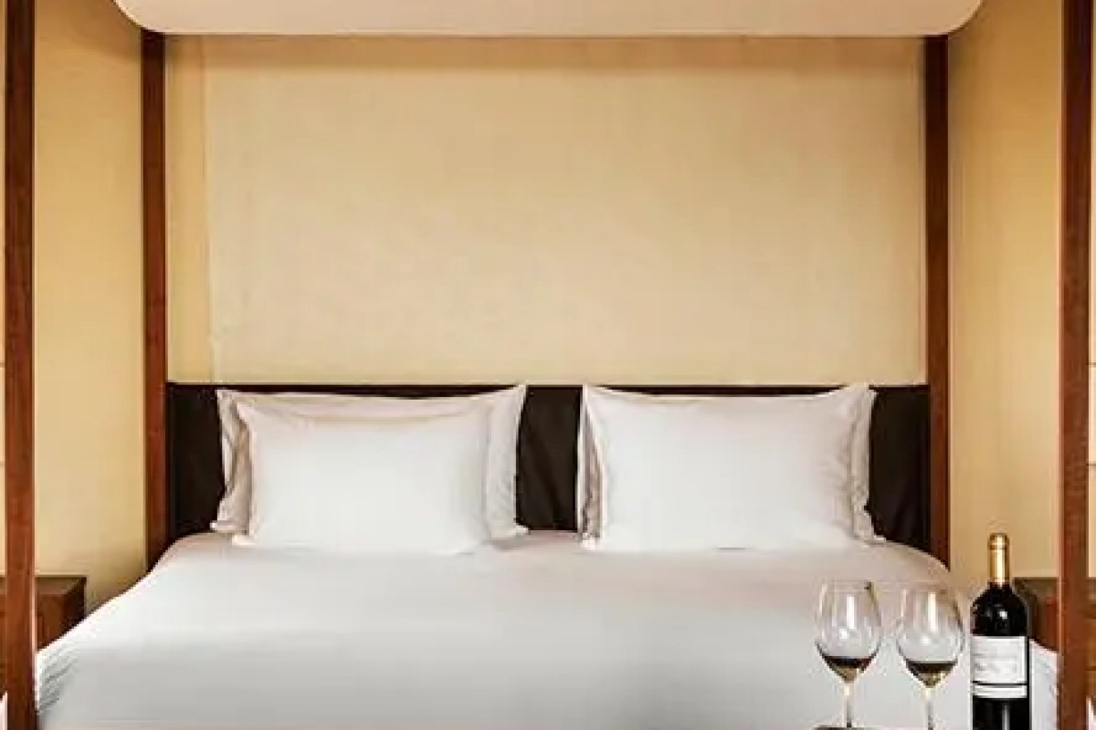 Close-up of four-poster bed with white linens and wine bottle with glasses