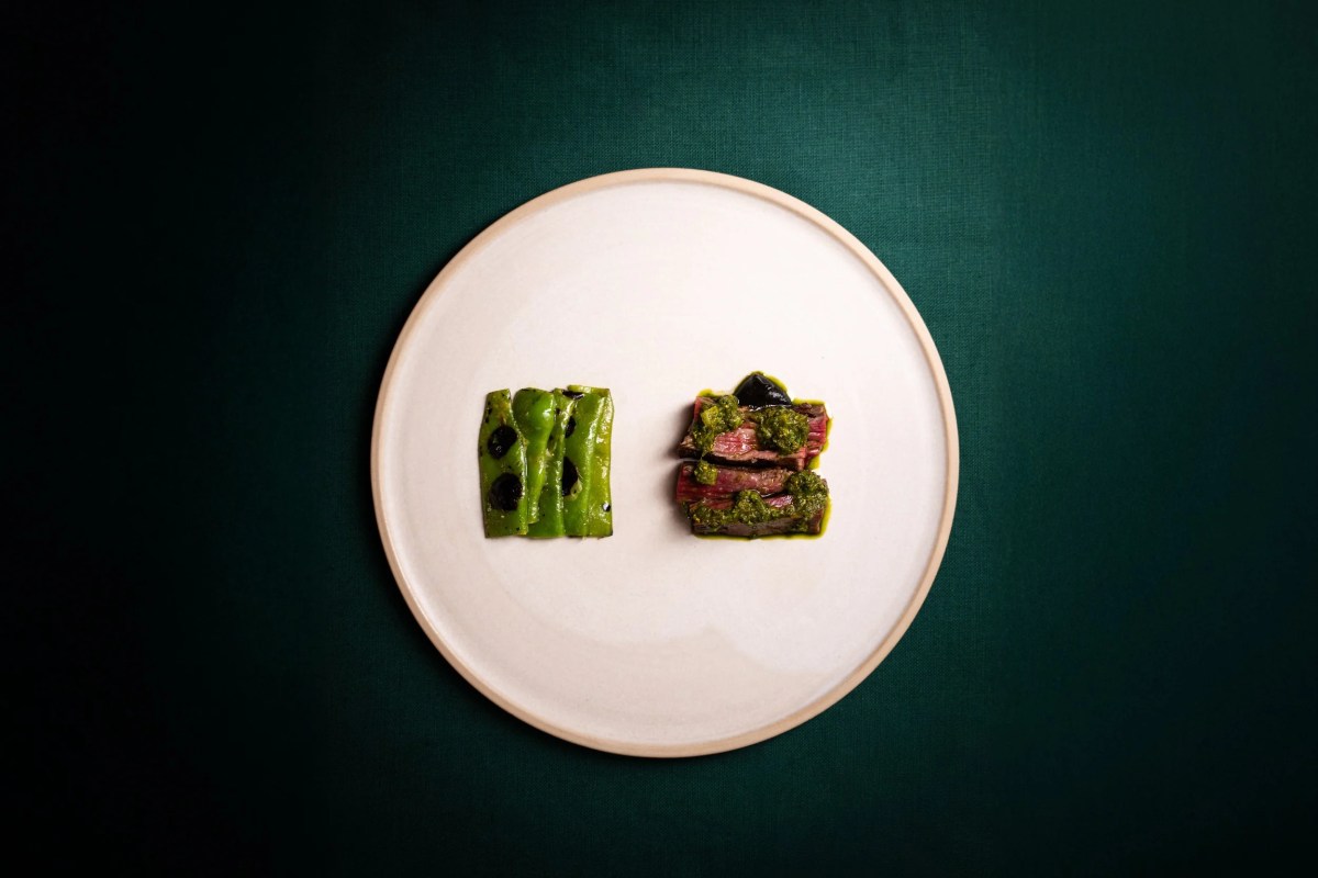 Overhead shot of a white plate with grilled green peppers and sliced steak with herb sauce on dark green background