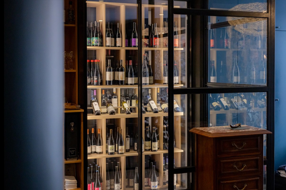 Glass-enclosed wine cellar shelving filled with bottles near a wooden cabinet