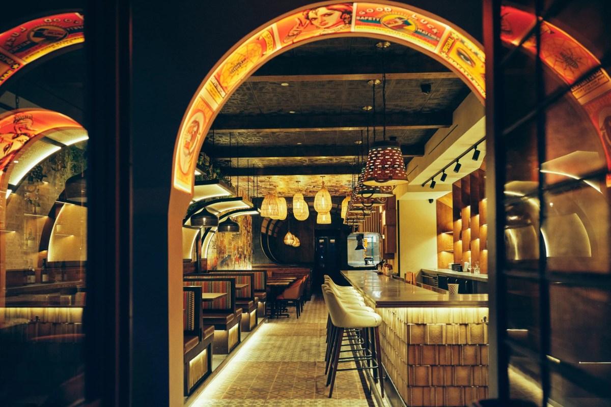 Interior view of Adda restaurant showing arched entryway, bar with stools, and dining booths under hanging lights