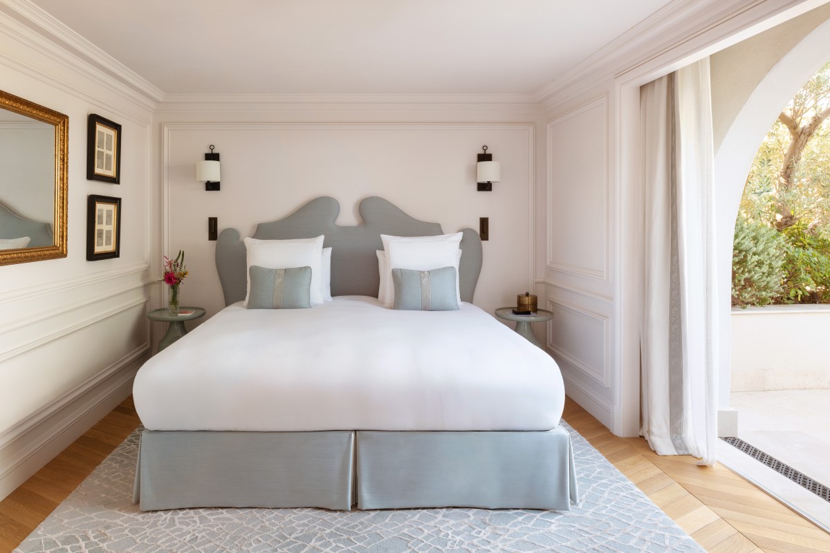 Elegant guest bedroom with grey upholstered headboard, white linens and garden view through arched doors