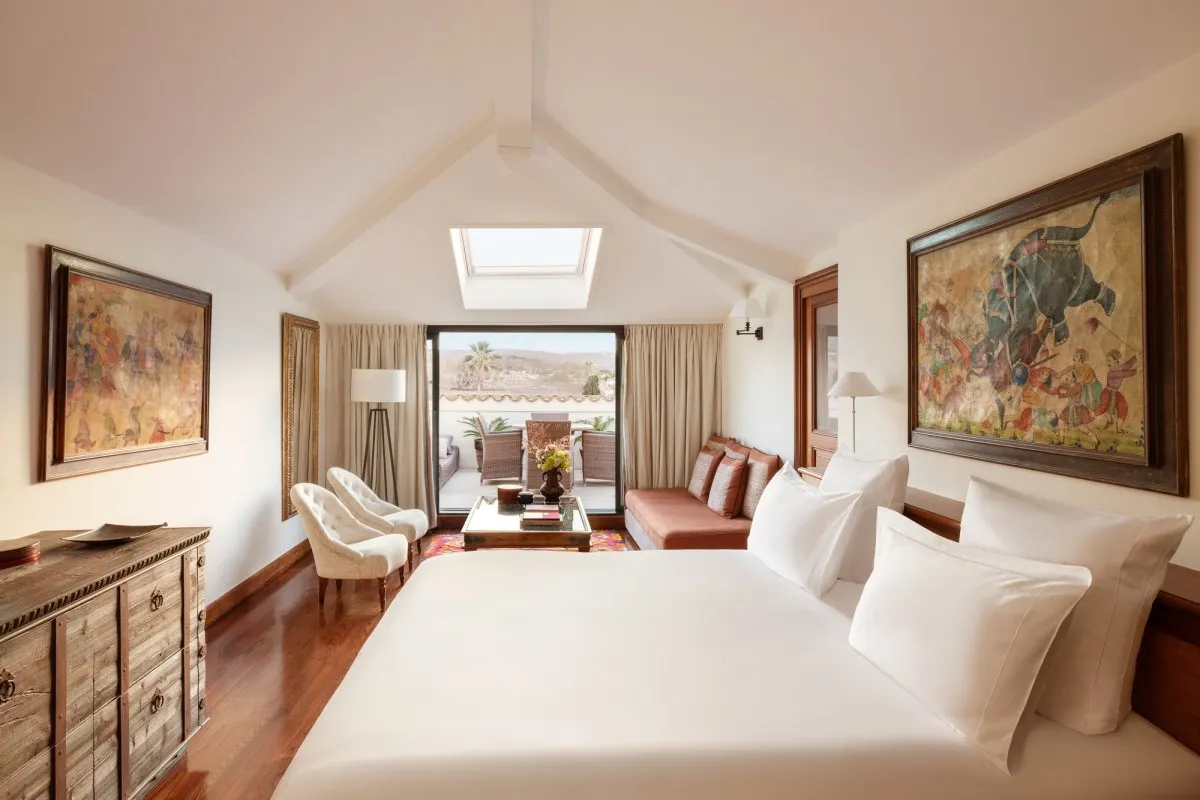 Bright guest suite with vaulted ceiling, skylight, large bed, seating area and terrace view
