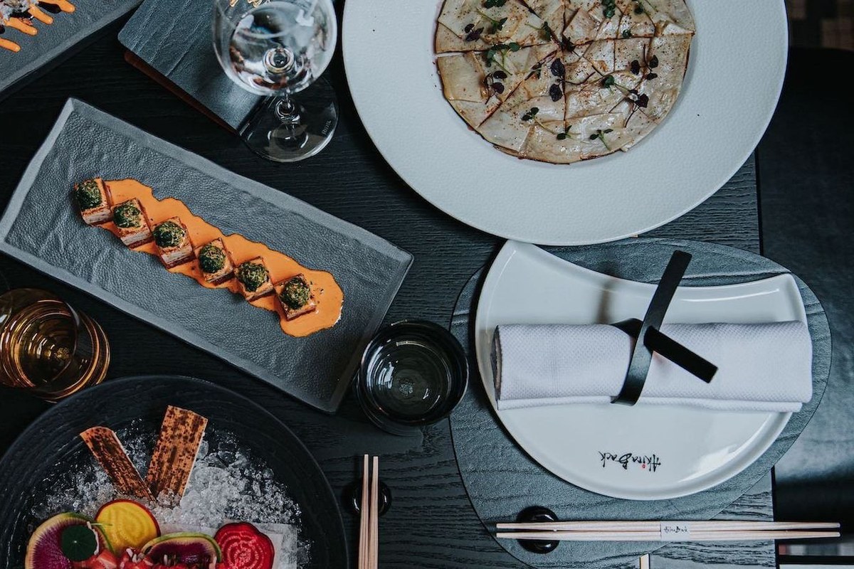 Overhead view of several Japanese-inspired dishes laid on a table with chopsticks and branded plate