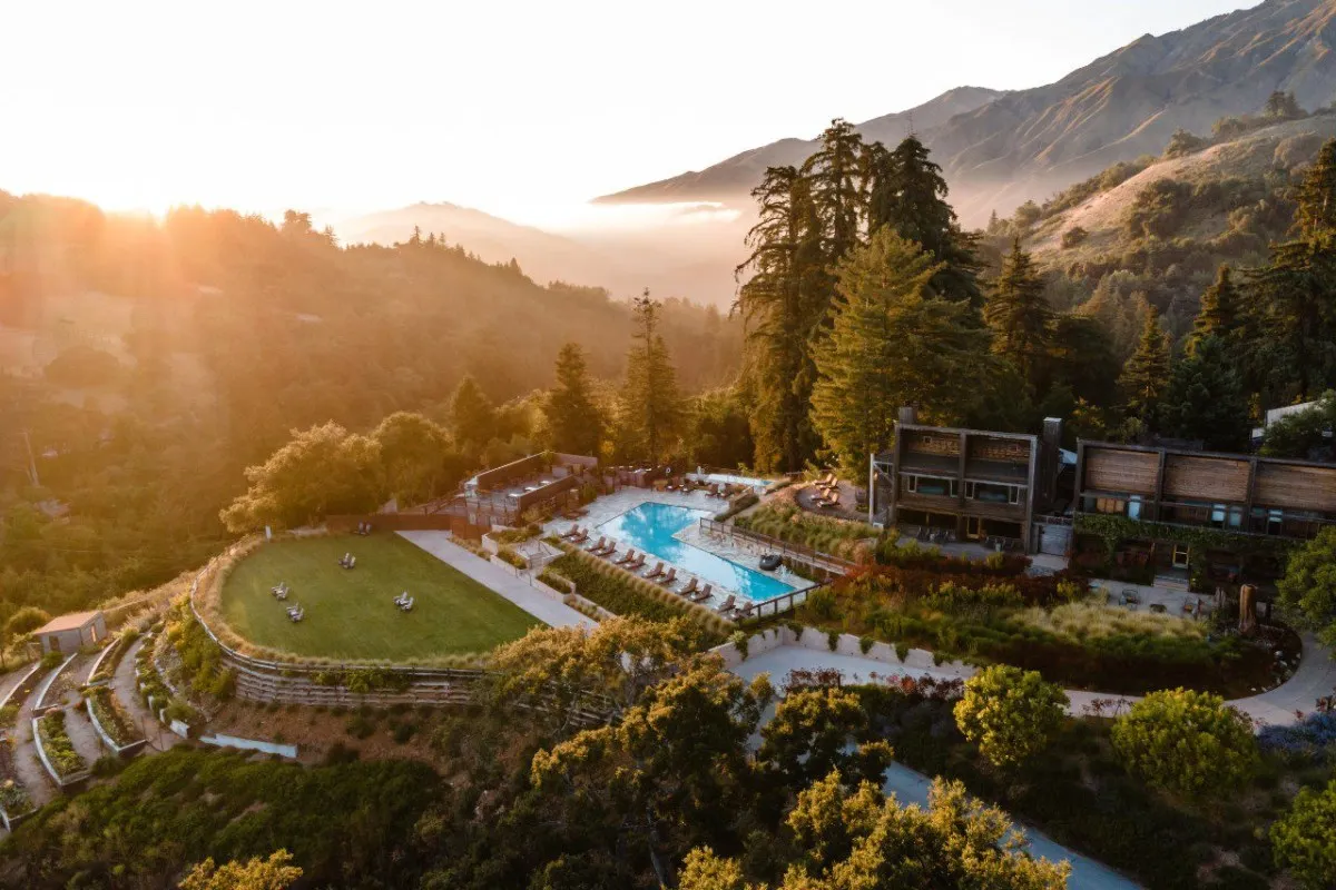 Aerial sunrise view of Alila Ventana Big Sur hotel buildings, pool and lawn nestled among trees and mountains