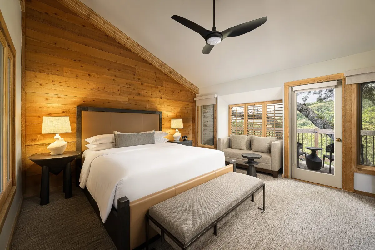 Spacious guest bedroom with wood accent wall, king bed, seating area and private balcony
