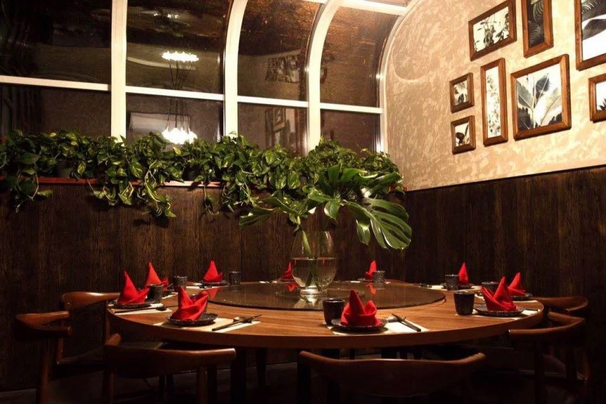 Round table set for dinner with red napkins under greenery and framed art