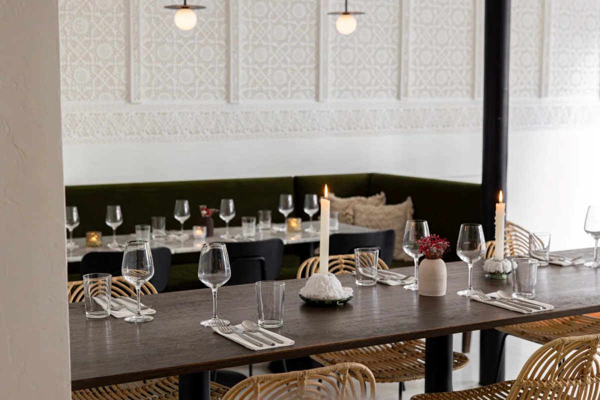 Restaurant dining room with set tables, candles, rattan chairs, and patterned white wall