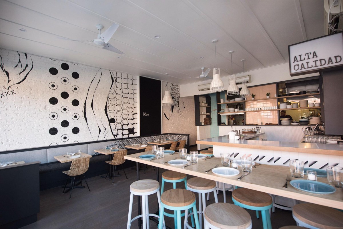 Interior dining room with Alta Calidad sign, patterned wall mural, and counter seating with blue stools