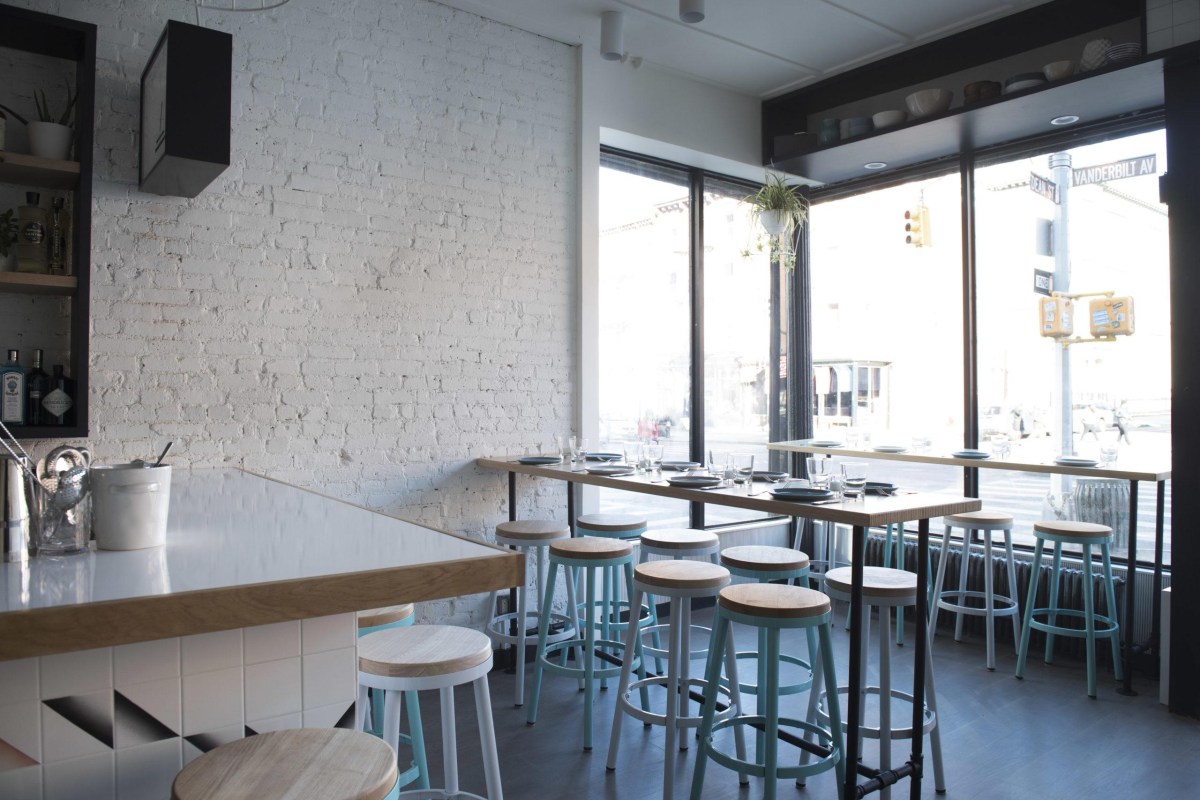 Dining counter by large windows overlooking Vanderbilt Ave intersection, white brick wall and bar area