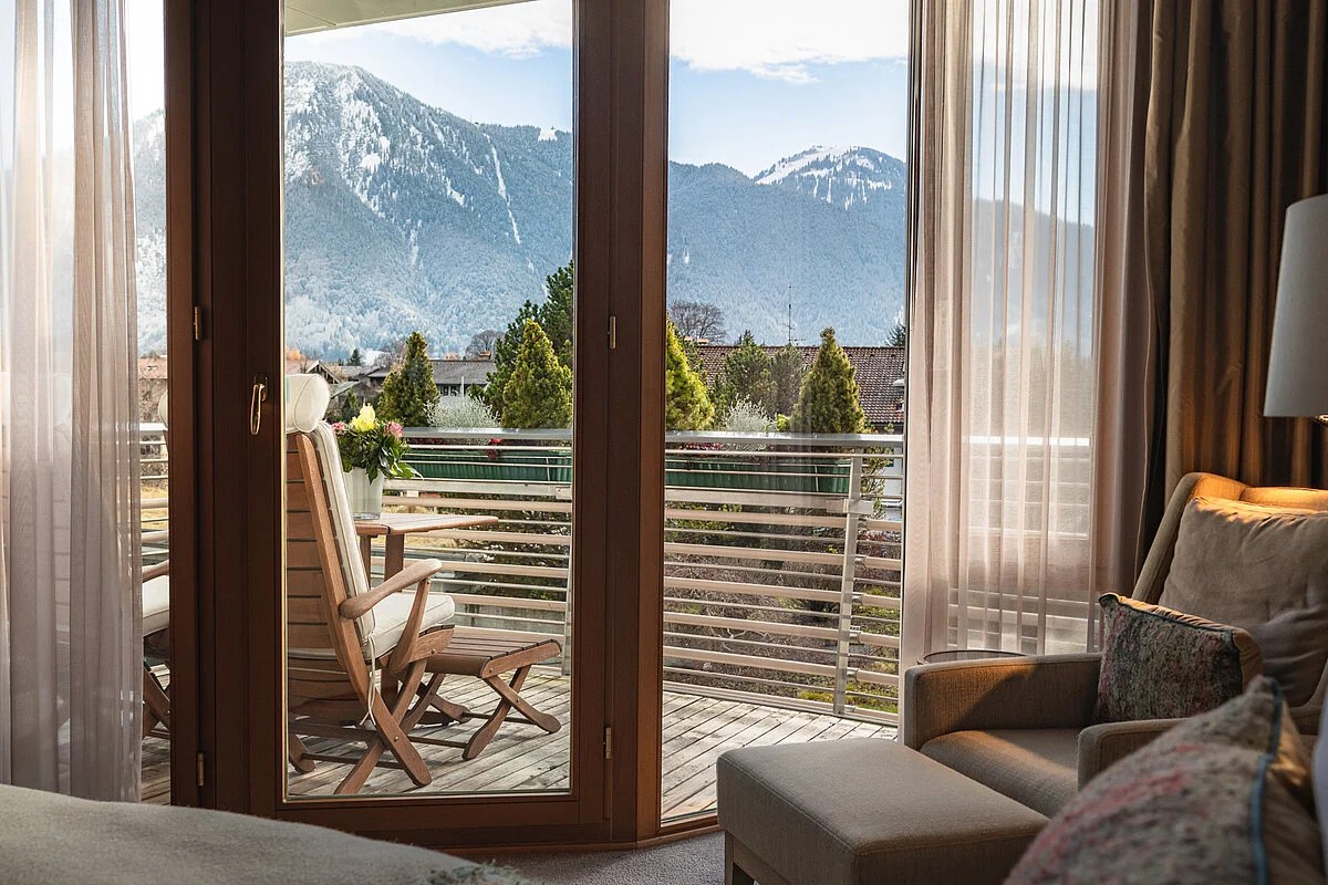 Hotel room with balcony doors open to a view of snow-capped Alps and trees