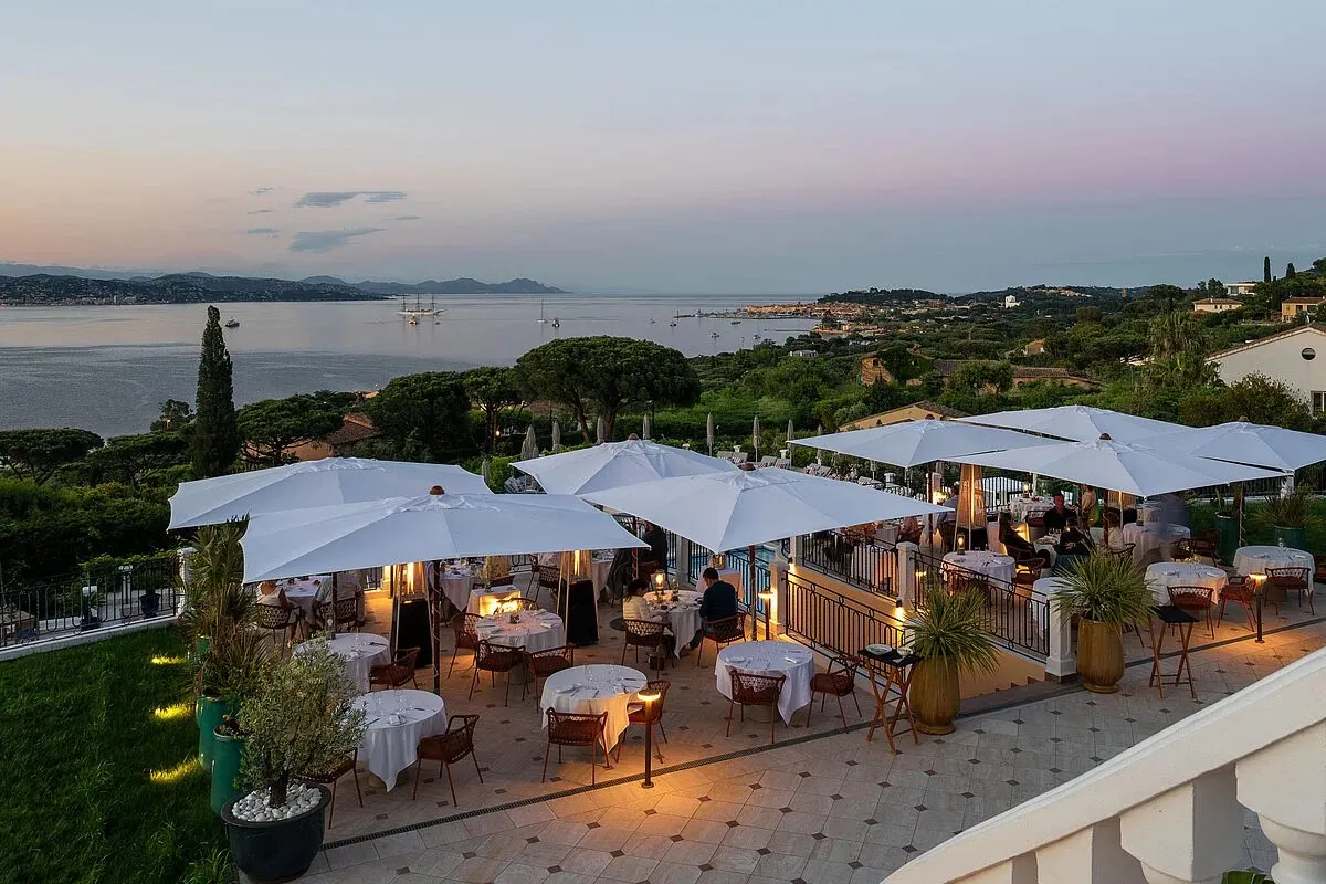 Hotel terrace restaurant at dusk with white umbrellas, set tables and panoramic sea view