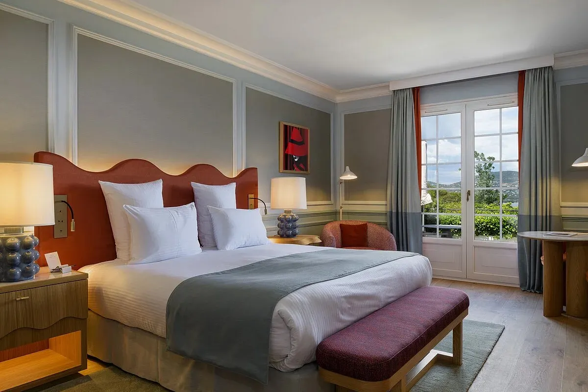 Elegant hotel guest room with red upholstered headboard, grey walls and French doors opening to a balcony view
