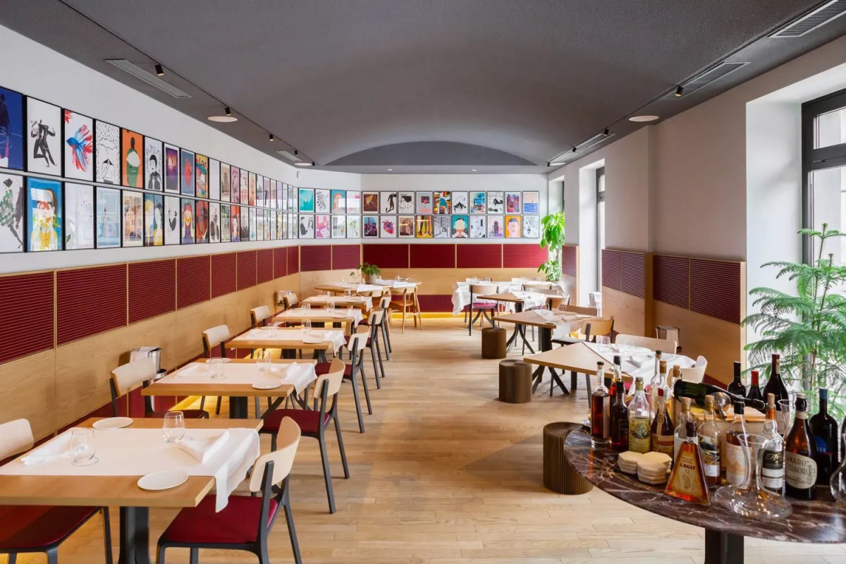Bright restaurant dining room with wooden tables, red accents, and gallery wall of art prints