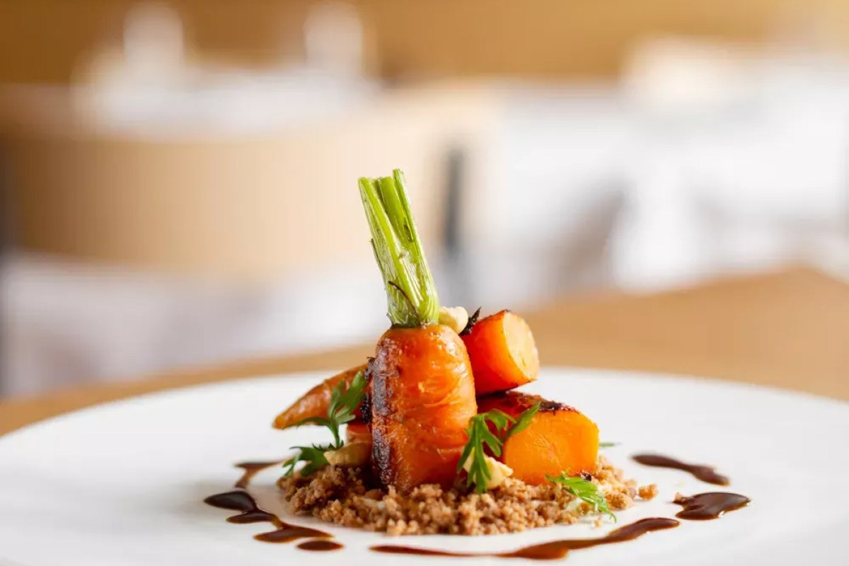 Plated dish of glazed roasted carrots with crumble and sauce drizzle on white plate