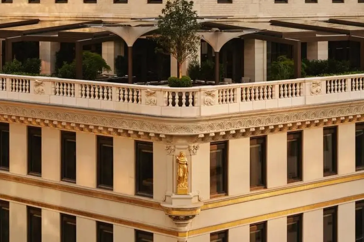 Close-up of Aman New York's ornate stone facade corner with gold accents and rooftop terrace garden visible above.