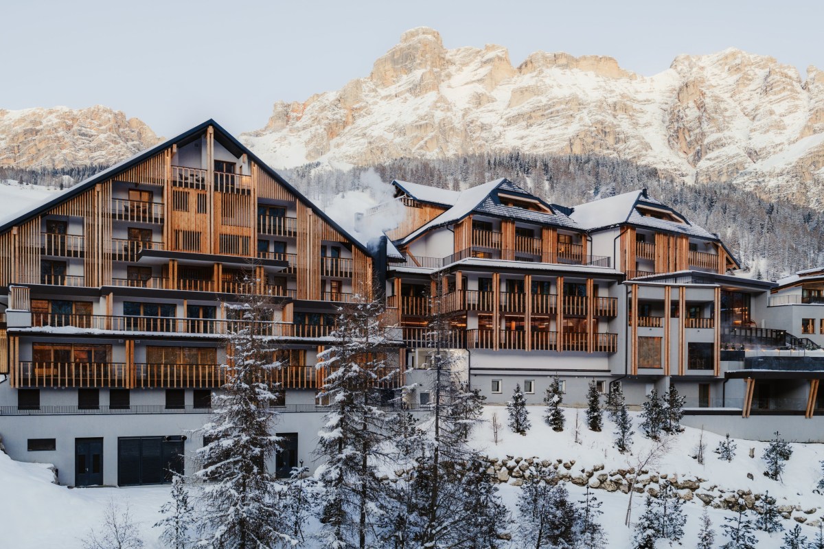 Wide exterior view of Aman Rosa Alpina's wood-and-stone facade at dusk with snow-capped Dolomites behind