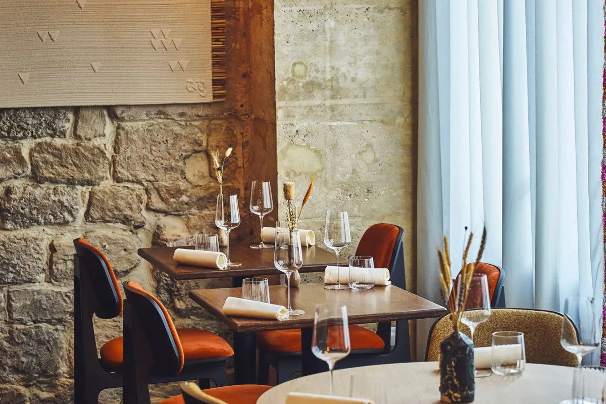 Elegant dining room with stone wall, wooden tables set with wine glasses, orange chairs, and sheer curtains