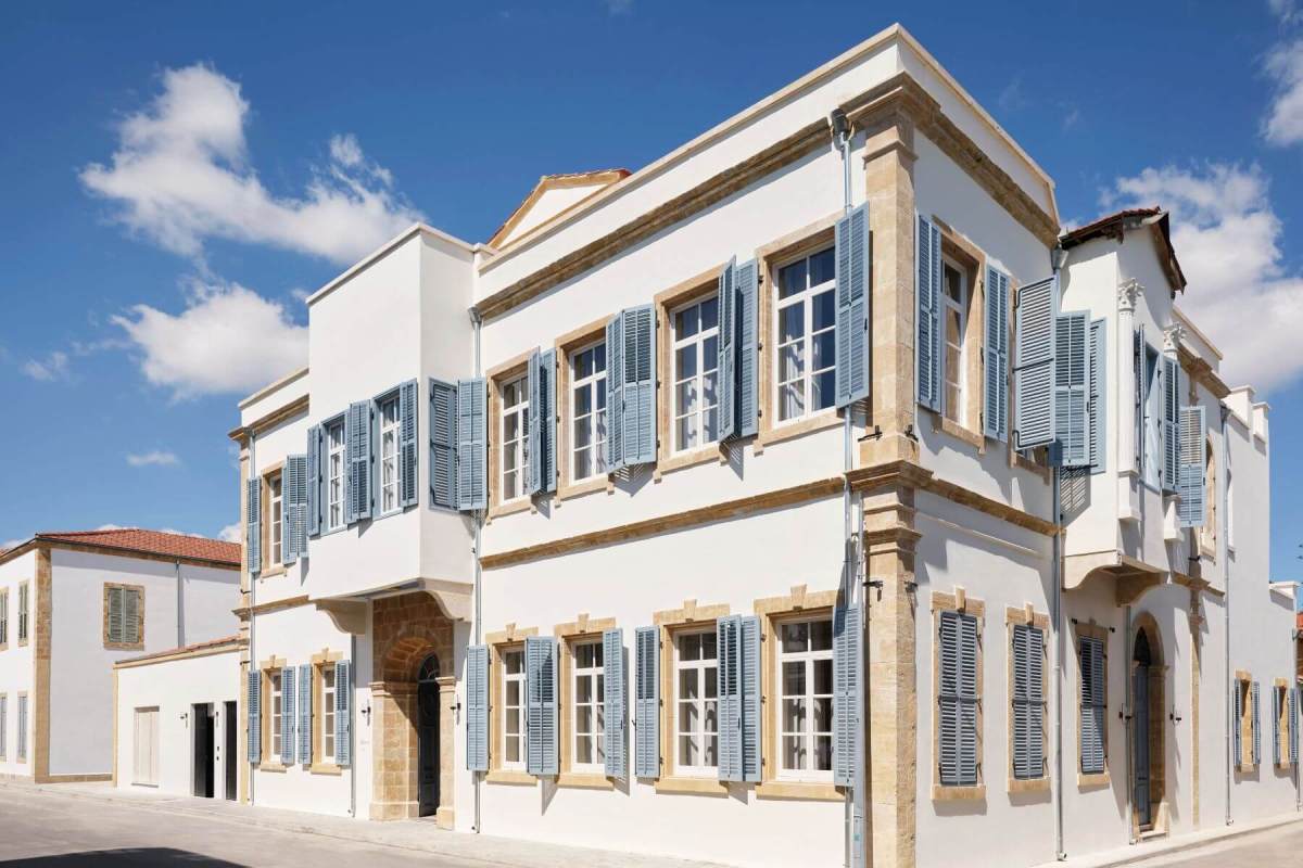 The white, two-storey façade of Amyth of Nicosia with pale blue shutters and stone-framed windows on a street in Nicosia's Old Town
