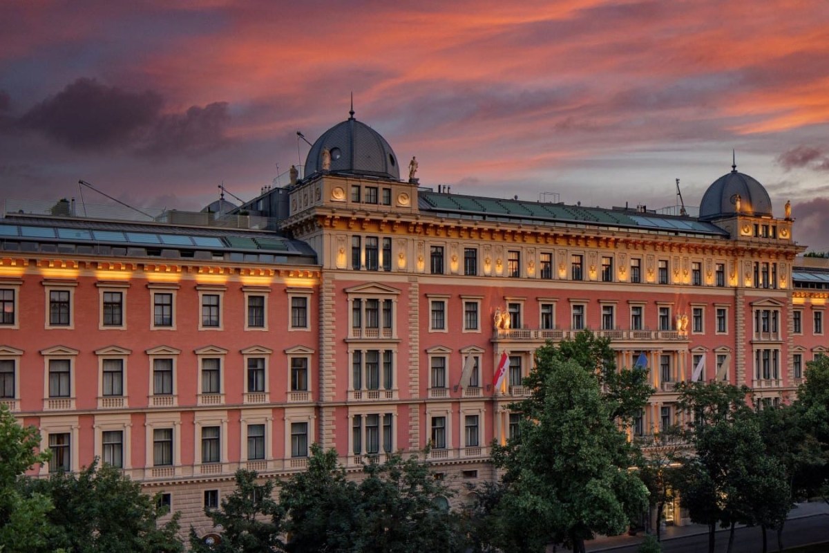 Grand historic hotel facade with twin domed towers under a dramatic sunset sky, trees lining the street below