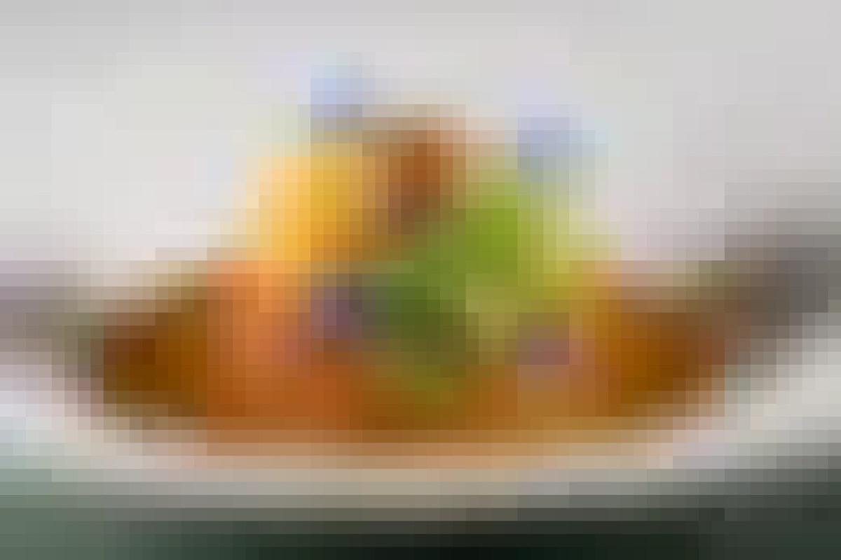 Blurry shot of a plated dish with orange, green, and tan components on a white plate