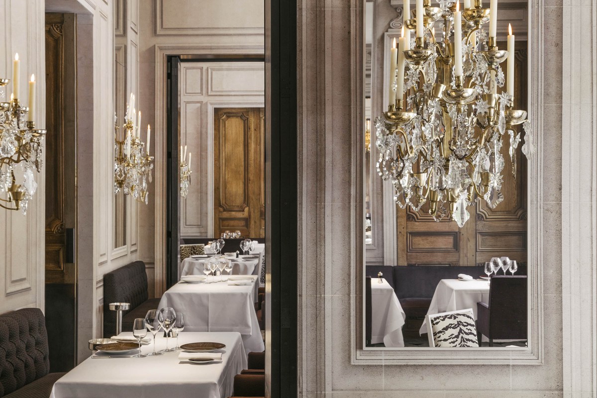 Elegant interior dining room with crystal chandeliers, wood paneling, and set tables reflected in a mirror.