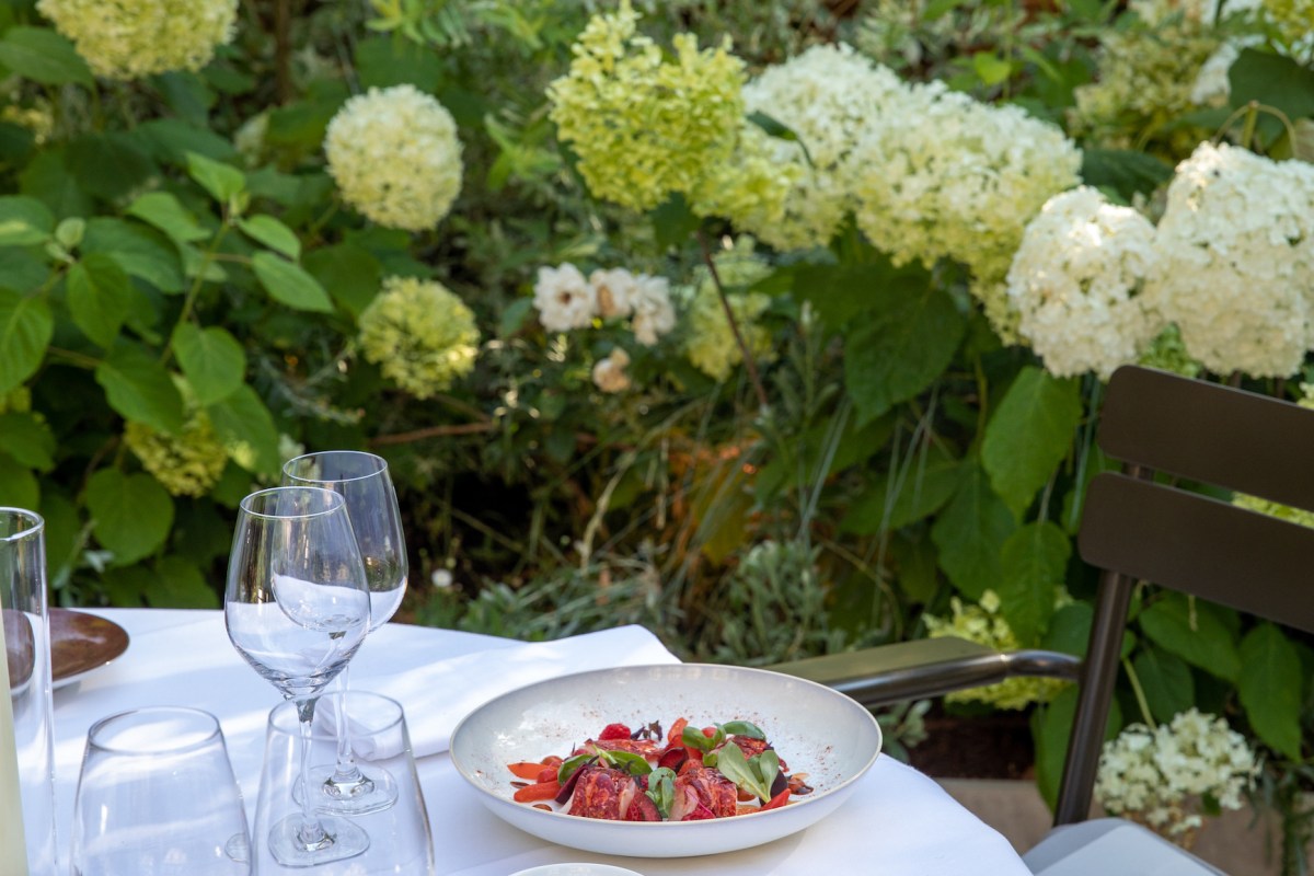 Beautifully plated dish on a white-clothed table set outdoors against lush hydrangea bushes.