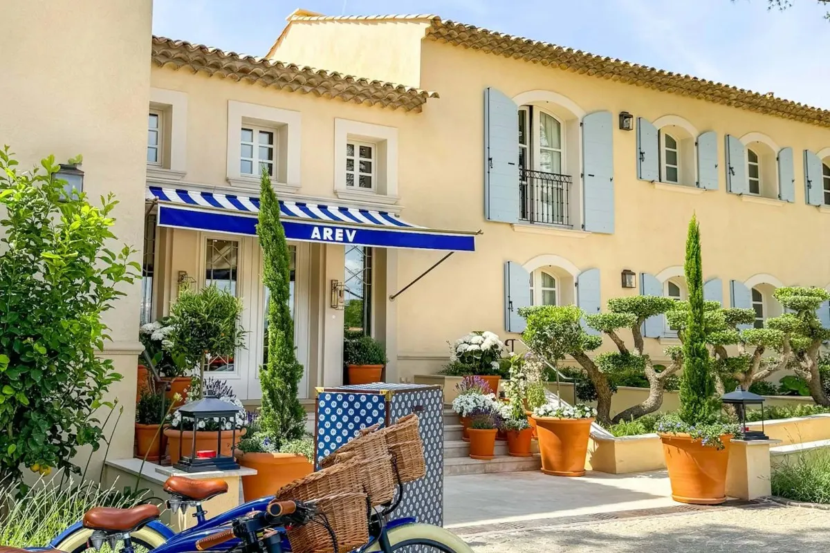 Front facade of Arev St. Tropez hotel with blue shutters, striped awning, and bicycles outside