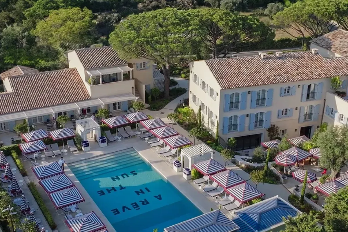 Aerial view of Arev hotel pool area with striped umbrellas, pool spelling 'A Rêve in the Sun', buildings surrounding