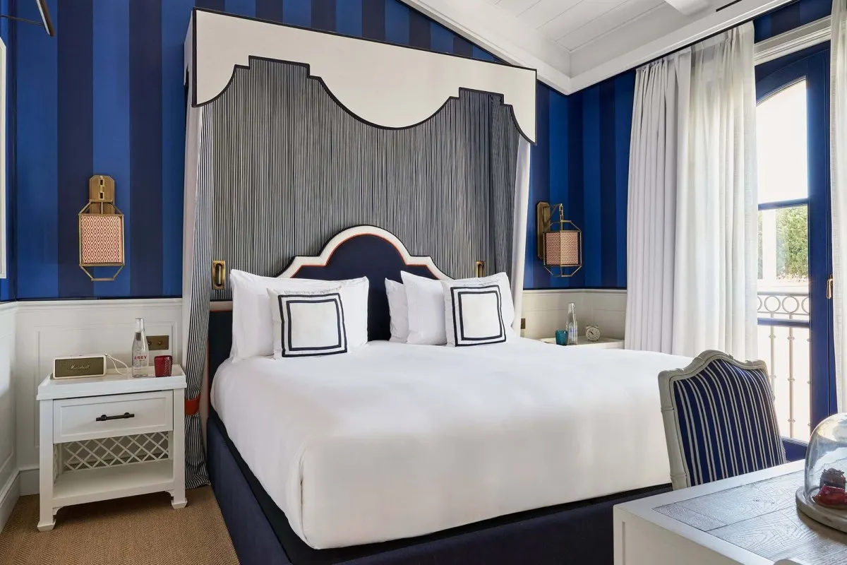 Hotel guest room with canopy bed in navy stripes, white linens, and balcony view