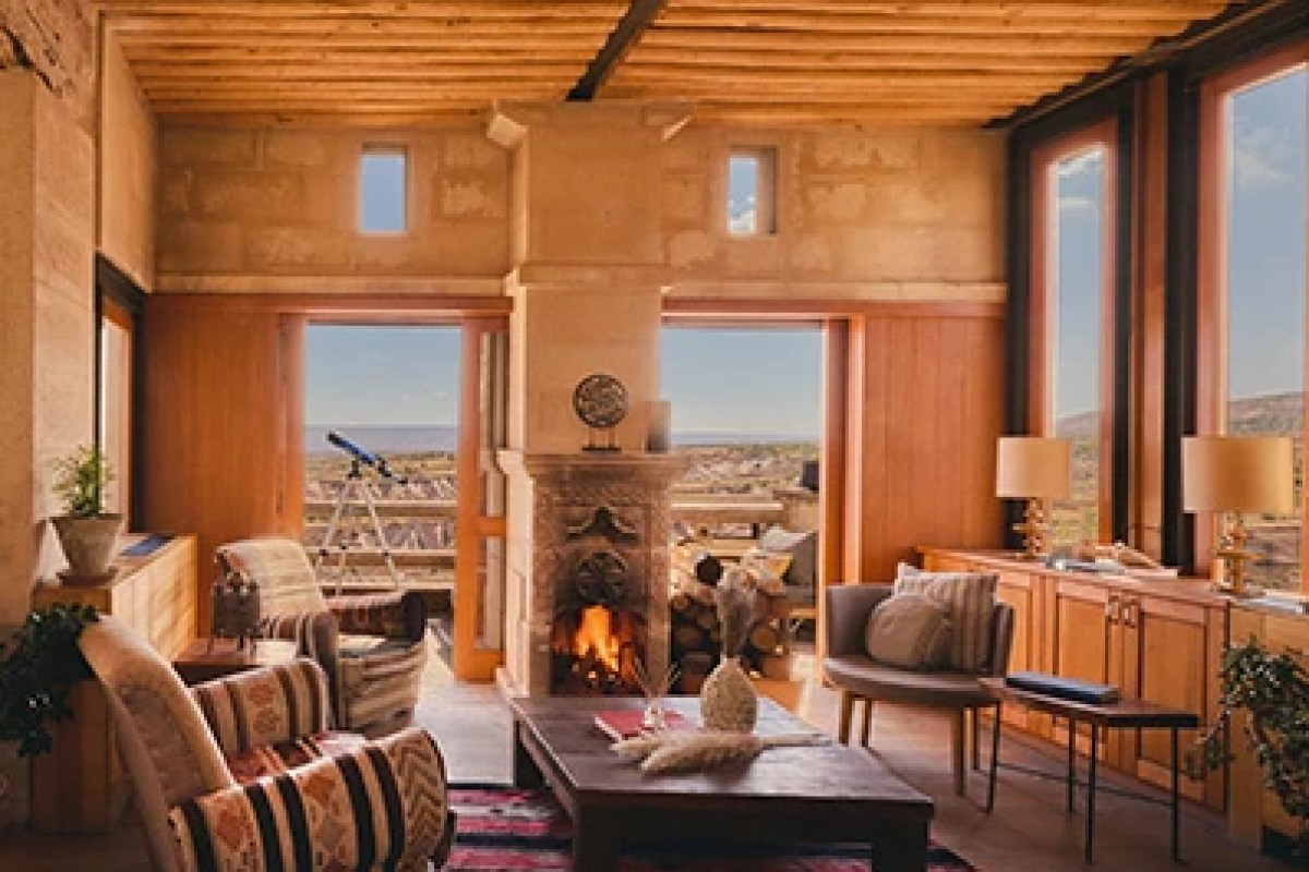 Hotel lounge with stone walls, fireplace, wooden beams, and valley view through open doors