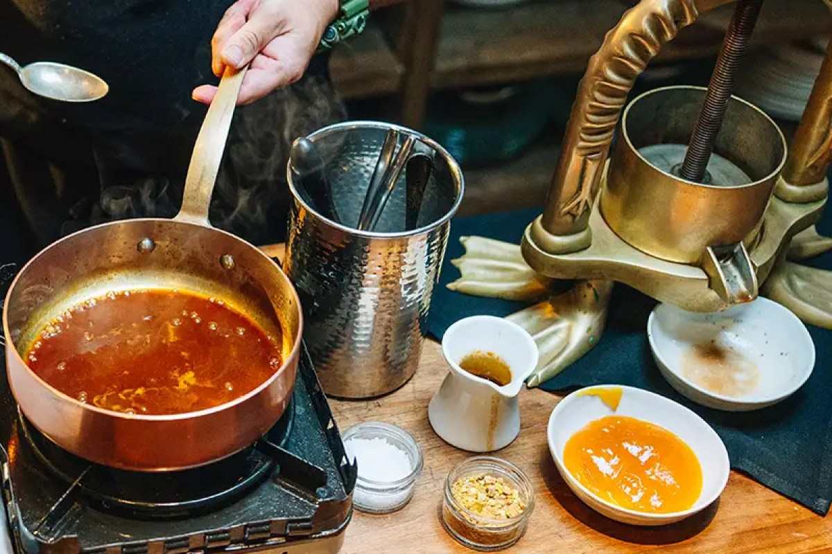 Kitchen prep scene with copper pan of sauce, citrus press, and condiment bowls