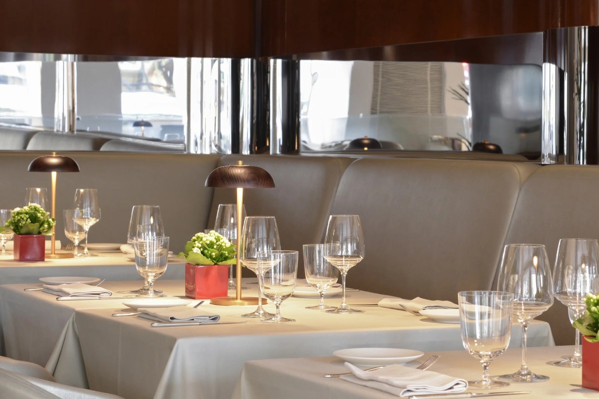 Restaurant dining room with set tables, wine glasses, flowers, and mirrored wall reflecting the street