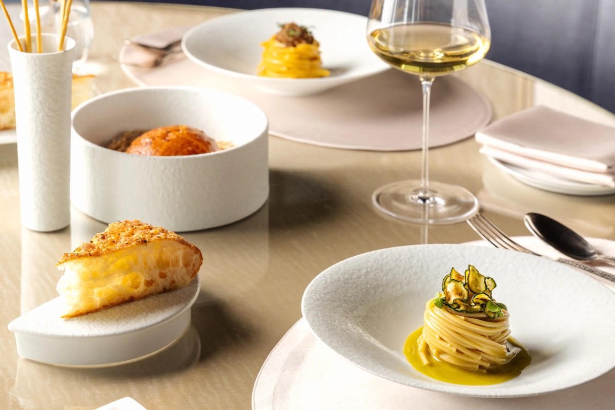 Gourmet pasta dishes with zucchini garnish, bread, and a glass of white wine on a restaurant table
