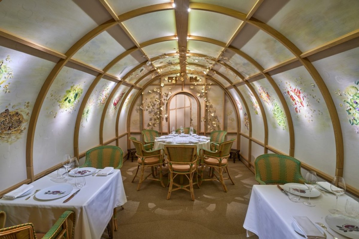 Arched glass-roofed dining room at Arpège with floral painted panels and set tables with wicker chairs