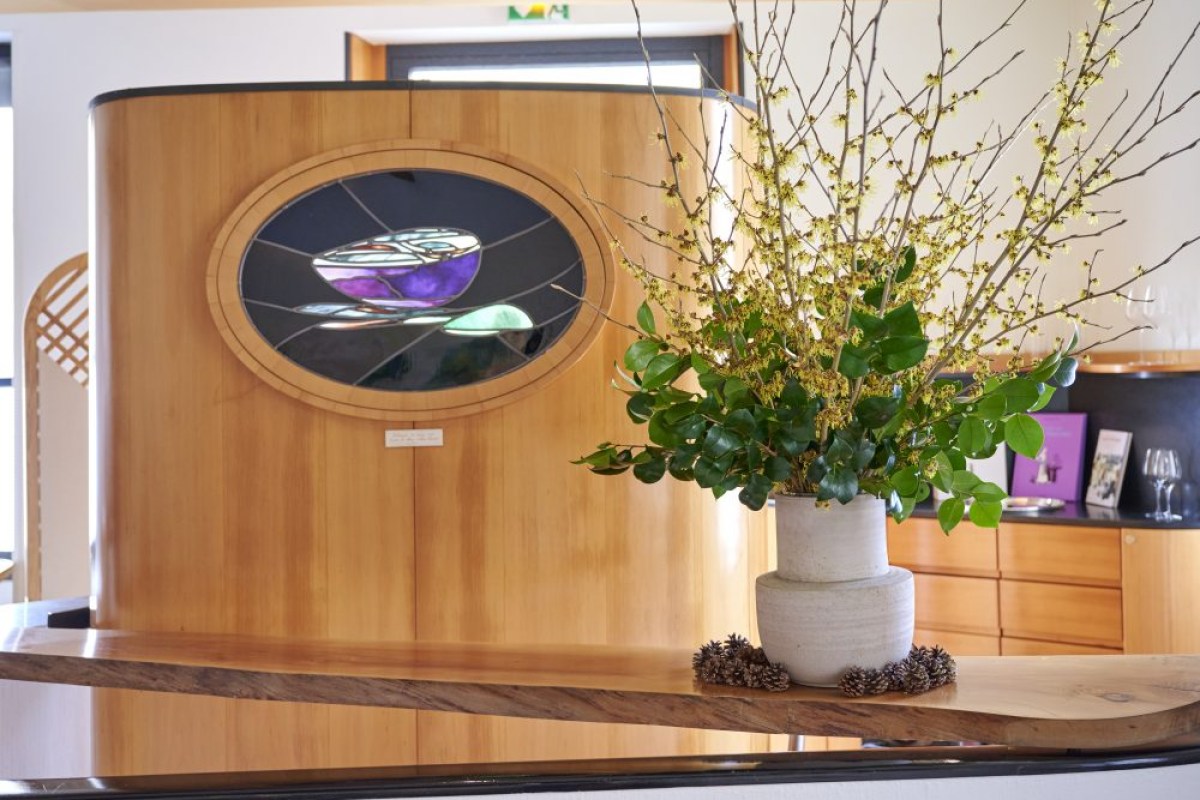 Arpège's reception area with a curved wood panel, stained-glass bowl motif, and a large flower arrangement on a wooden bar