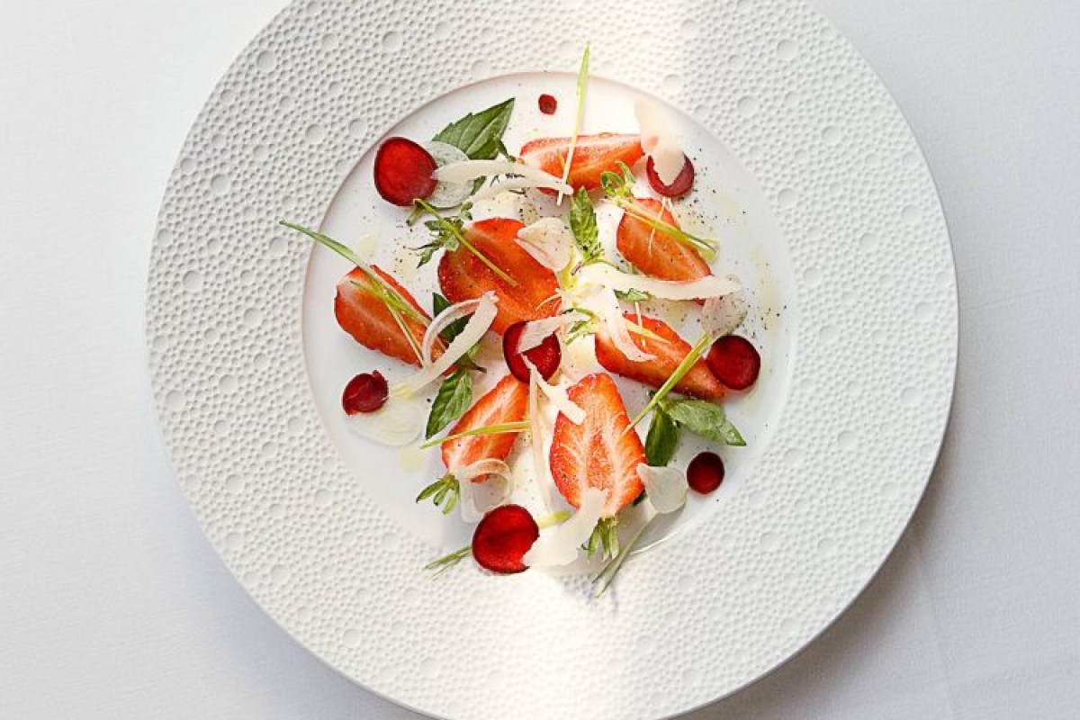 A refined plated dish at Arpège featuring sliced strawberries, radish, herbs, and shaved cheese on a textured white plate