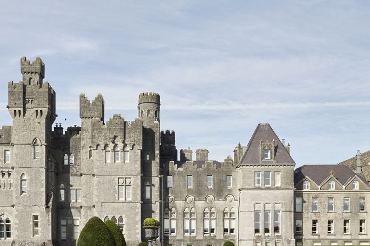 Wide view of Ashford Castle's stone facade with turrets and windows under a pale sky