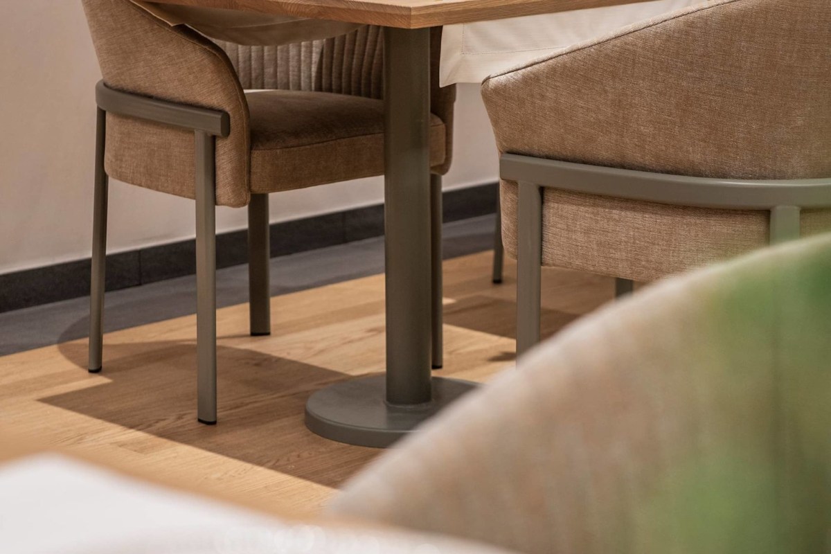 Close-up of dining room chairs and table legs on wooden floor with green plant blur