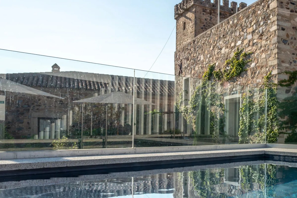 Glass-fenced rooftop pool with reflection, overlooking the stone castle tower and tiled roof of Atrio hotel.