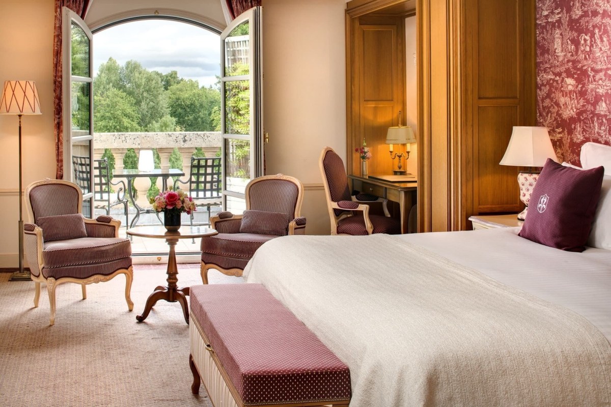 Luxury hotel guest room with striped armchairs, bed, and open doors to a balcony with garden view