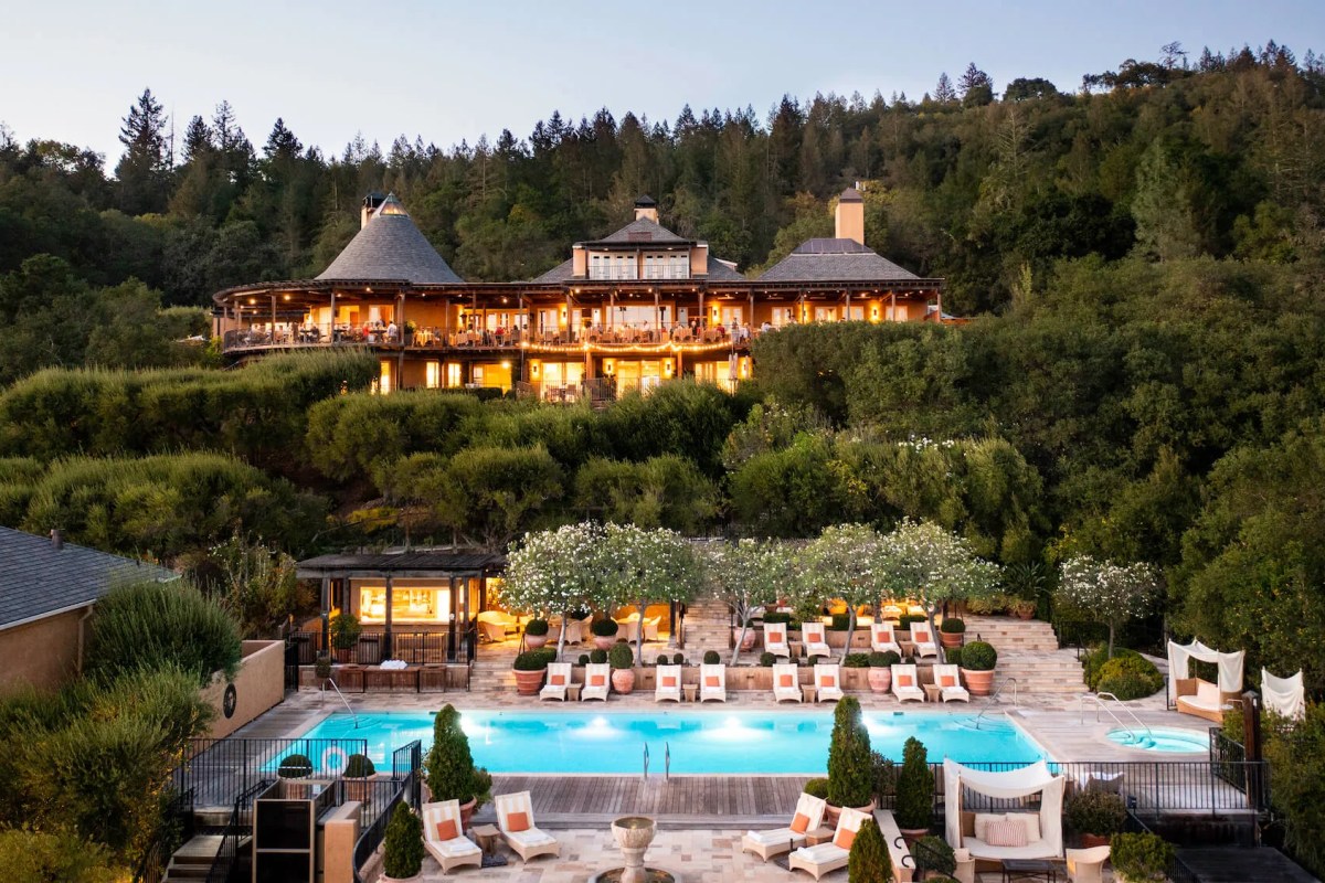 Aerial dusk view of Auberge du Soleil's hillside lodge with lit terraces overlooking a glowing pool and lounge chairs.
