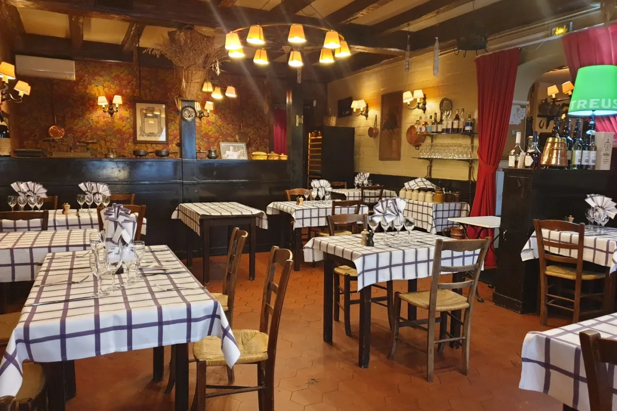 Interior dining room with wooden beams, chandelier, bar, and tables set with checked purple-and-white tablecloths and wine glasses